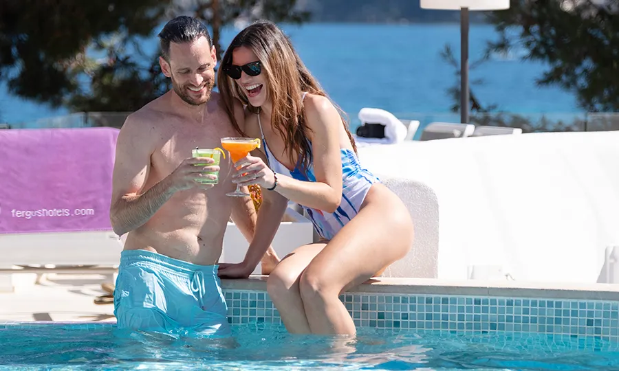 Pareja brindando sentados al borde de una piscina